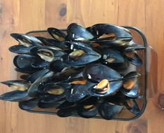 a basket filled with lots of mussels on top of a wooden table