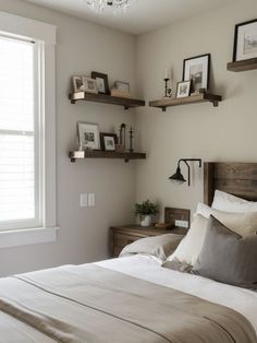 a bed with white sheets and pillows in a bedroom next to a window filled with framed pictures