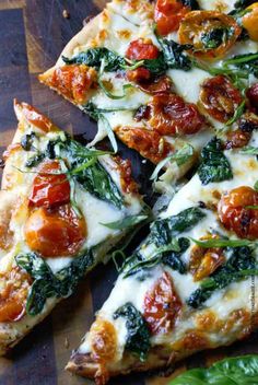 several slices of pizza on a wooden cutting board with basil leaves and tomatoes in the background