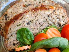 a glass bowl filled with meat, tomatoes and spinach on top of a table