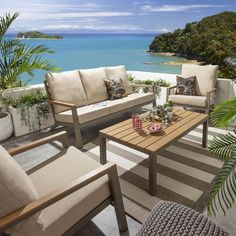 an outdoor living area with couches, tables and chairs overlooking the ocean on a sunny day