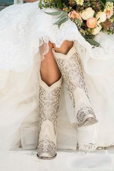 a woman in cowboy boots and wedding dress with flowers on her head is sitting down