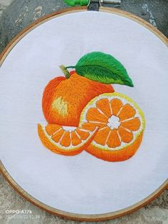 an embroidery project with oranges and green leaves on white fabric, sitting on top of a rock