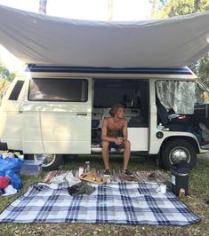 a shirtless man sitting in the back of a camper van under a tarp