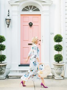 a woman is walking in front of a pink door