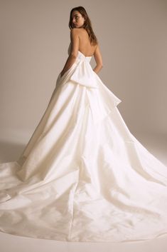 a woman in a white wedding dress standing on a white surface with her back turned to the camera