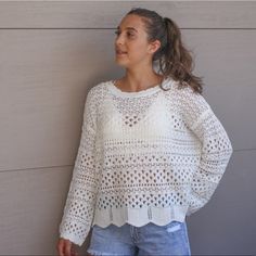 a woman standing in front of a wall wearing a sweater with crochet on it