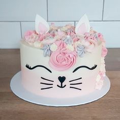 a white cake with pink flowers and cat's face on top, sitting on a wooden table