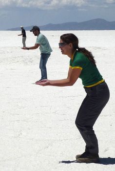 a woman catching a frisbee in the middle of an empty field with two men standing behind her