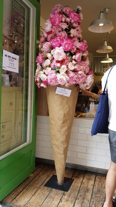 there is a large vase with pink flowers on display in the store front window and people are looking at it