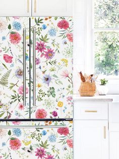 a white kitchen with colorful floral wallpaper on the refrigerator and side by side cabinets