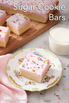 sugar cookie bars with pink frosting and sprinkles on a plate next to a glass of milk