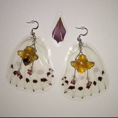 pair of white and brown glass earrings with yellow flowers on them, hanging from hooks