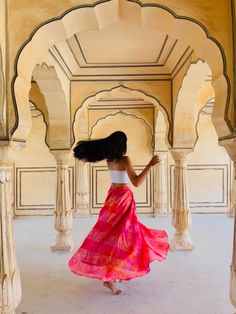 a woman in a red and pink dress walking through an archway