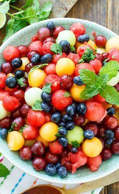 a bowl filled with watermelon, blueberries and cucumber on top of a wooden table