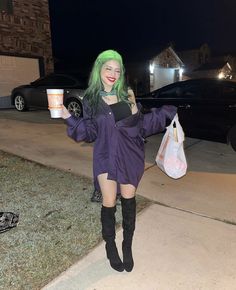 a woman with green hair is walking down the sidewalk while holding a cup in her hand