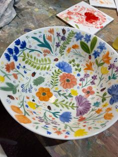 a bowl with flowers painted on it sitting on a table next to other art supplies