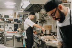 two men in a kitchen preparing food on top of stoves and pans with utensils