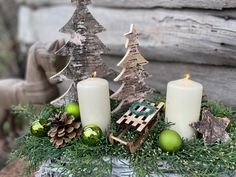 two candles sitting on top of a table next to christmas decorations and ornaments in front of a log cabin