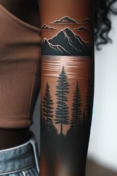 a woman with a tattoo on her arm is standing in front of a mountain and trees