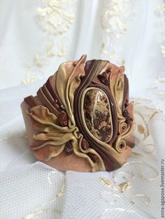 a close up of a bracelet on a white cloth with gold and brown decorations around it