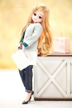 a doll with long blonde hair is standing next to a white box and holding a purse