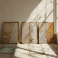 three framed paintings sitting on top of a tiled floor next to a window in an empty room