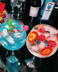 two glasses filled with different types of drinks on top of a table next to bottles