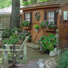 a small wooden shed with flowers in the window boxes on the side and chairs around it