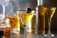 two martini glasses filled with yellow liquid and olives