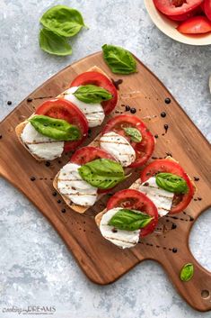 sliced tomatoes and mozzarella on a wooden cutting board with basil leaves around them