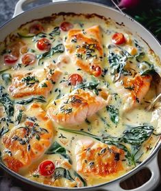 a pan filled with chicken and spinach covered in cheese, sauce and tomatoes on top of a wooden table