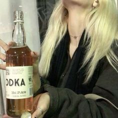 a blonde woman holding a bottle of vodka in her hand and looking up at the sky