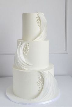 a three tiered white wedding cake with pearls