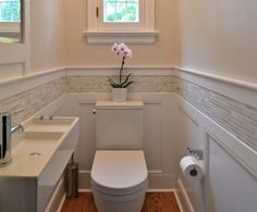 a white toilet sitting in a bathroom next to a sink under a window with a potted plant on top of it