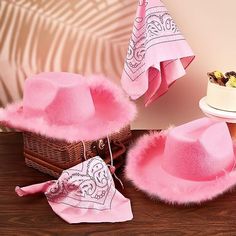 a pink hat and other items on a wooden table next to a basket with cake