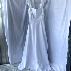 a white dress hanging on a clothes rack in front of a window with curtains behind it