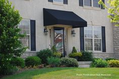 a white house with black awnings and bushes