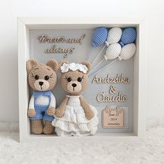 two crocheted teddy bears are in a shadow box with balloons on the wall