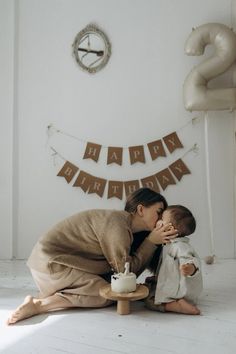 a woman kissing a baby on the cheek in front of a happy birthday banner and bunting