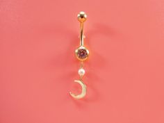 a gold belly ring with a crescent and pearls hanging from it's side on a pink background