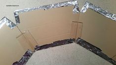 an open cardboard box sitting on the floor with tin foil covering it's sides