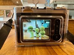 a digital camera sitting on top of a wooden table with two stuffed animals in front of it