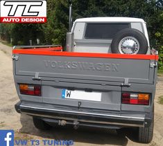 the back end of a grey truck parked on top of a dirt road next to trees