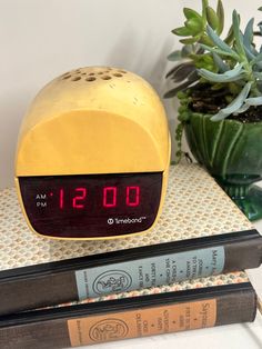 a yellow alarm clock sitting on top of two books next to a potted plant