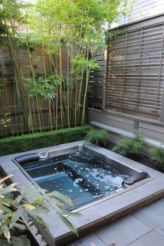 an outdoor hot tub in the middle of a garden with bamboo trees and bushes behind it