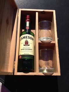 a bottle of jameson in a wooden box with two shot glasses on the table next to it