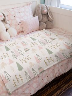 a bed with pink and green christmas trees on it, next to a stuffed animal