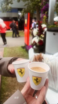 two cups of coffee are being held by someone's hand at an outdoor event