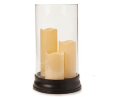 three candles in a glass container on a black stand against a white background with no one around them